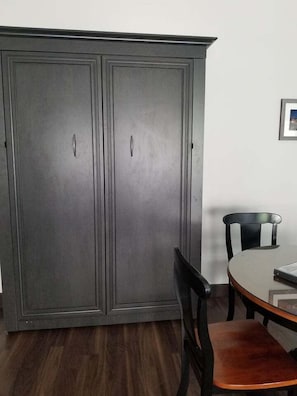 A room with a dark wooden wardrobe, a dining table with chairs, and a framed picture on the wall. - La Digue Suites  (Cheticamp)