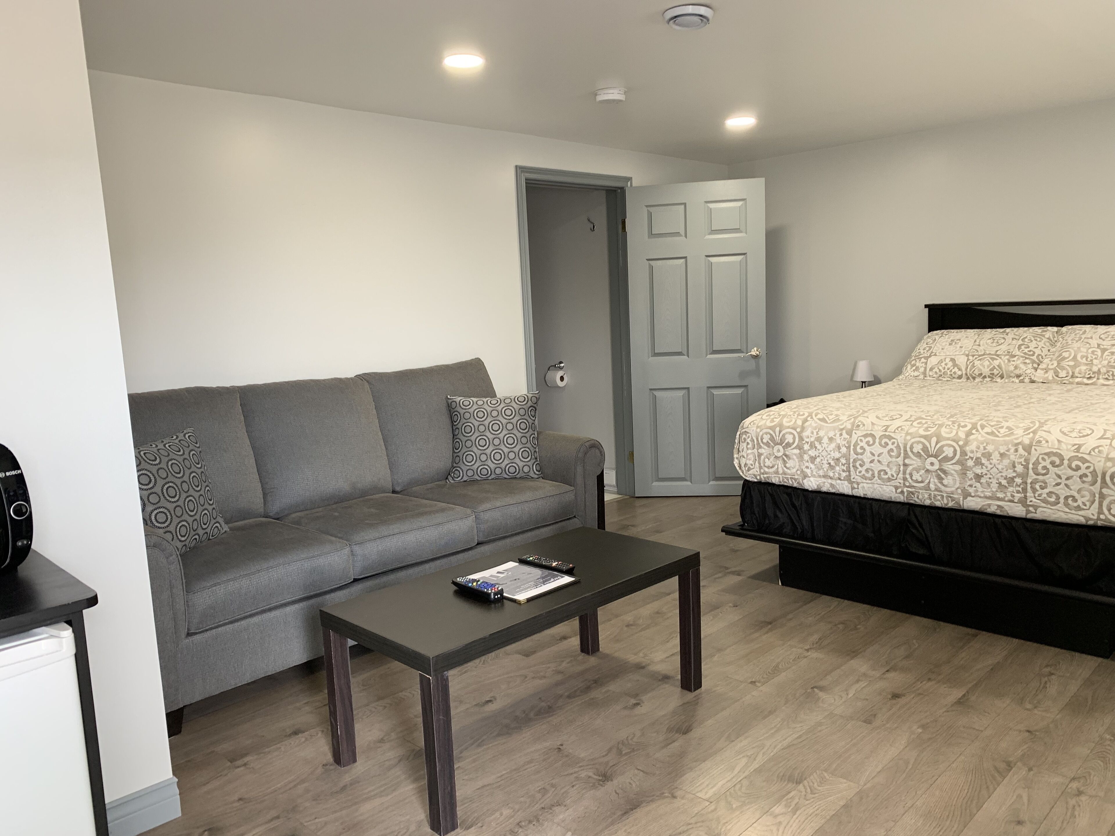 A bedroom with a bed, a grey sofa, a small table, and a door.