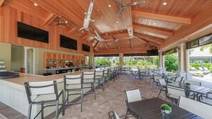 A covered outdoor dining area with a bar, wooden ceiling, and large windows overlooking a garden. - Esplanade on Palmer Ranch - Luxury, Brand-New, Clubhouse, Resort-Style Pool, ++ (Sarasota)