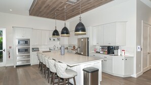 A spacious kitchen with white cabinetry, a central island with bar stools, stainless steel appliances, and pendant lighting. - Esplanade on Palmer Ranch - Luxury, Brand-New, Clubhouse, Resort-Style Pool, ++ (Sarasota)