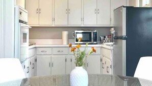 A modern kitchen with white cabinets, a black refrigerator, a microwave, and a glass table with a white vase of flowers.