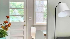 A room with a gray sofa, a white lamp, a teal vase with flowers, and a door leading to another room.