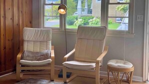 A room with two upholstered chairs, a small round stool, and a floor lamp.