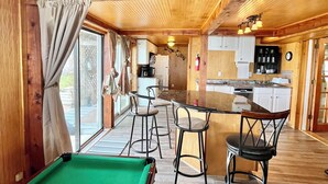 Un intérieur en bois avec une table de billard, des tabourets de bar et un coin cuisine.