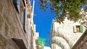 A narrow stone-paved alleyway with buildings on either side, a bicycle with a basket, and a clear blue sky.