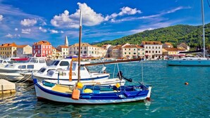 A marina with boats docked, a clear blue sky, and buildings with red roofs in the background.