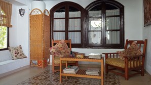 A cozy room with a wooden ceiling, a woven chair, two wooden chairs with cushions, a small table with books, and a window with curtains. - La Casita Verde Valle (Unknown)