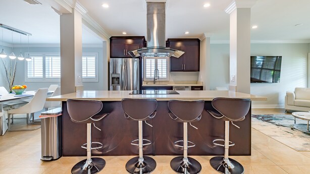 A modern kitchen with a central island, bar stools, stainless steel appliances, and a large window.