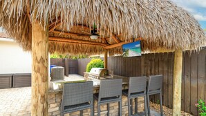 An outdoor patio with a thatched roof, stone bar counter, and wicker chairs.