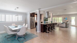 A spacious kitchen with a central island, a dining area with a white table and chairs, and a living area with a sofa and a coffee table.