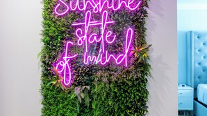 A wall with a vertical garden and a neon sign that reads "Sunshine state of mind."