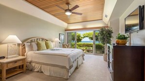 A bedroom with a large bed, a wooden ceiling fan, a TV, and a view of the ocean through large windows. - Puunoa Beach Estates- Part OF Hyatt (LAHAINA)
