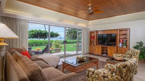 A spacious living room with a large TV, comfortable seating, and a view of the outdoors. - Puunoa Beach Estates- Part OF Hyatt (LAHAINA)