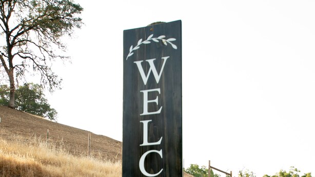 A wooden sign with the text "WELCOME TO OUR FARM" on a dirt road.