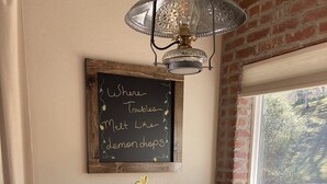 A round wooden table with a vase of yellow flowers, two chairs, a chalkboard with writing, and a brick wall with a window. - Romantic Private Getaway!  Hot tub, Fireplace and Views!  (Hopland)