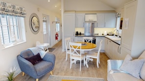 Une cuisine moderne avec des meubles blancs, un îlot central et un coin repas comprenant une table ronde et des chaises blanches.