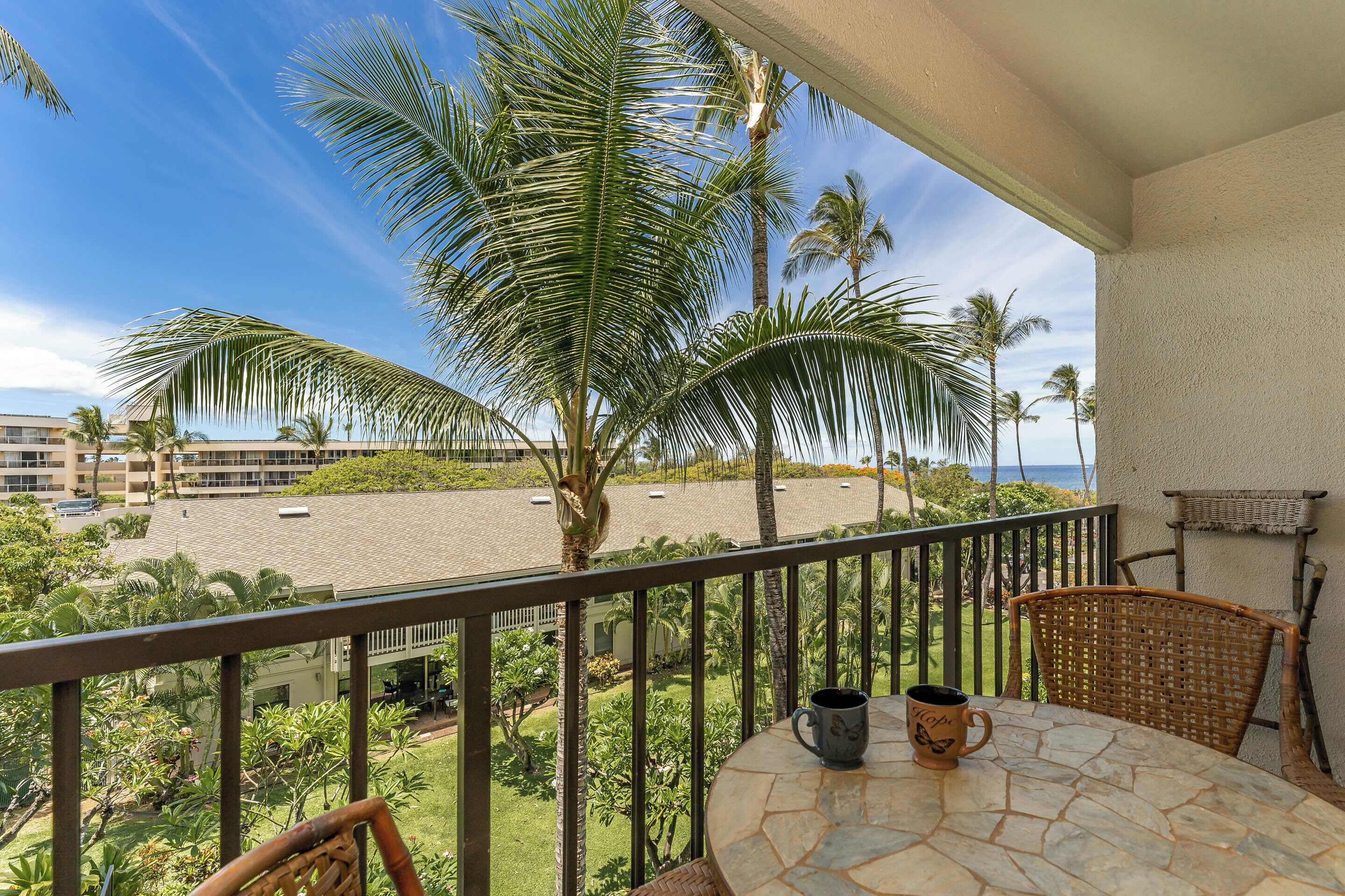A balcony with a view of a landscaped area, palm trees, and a building in the background.