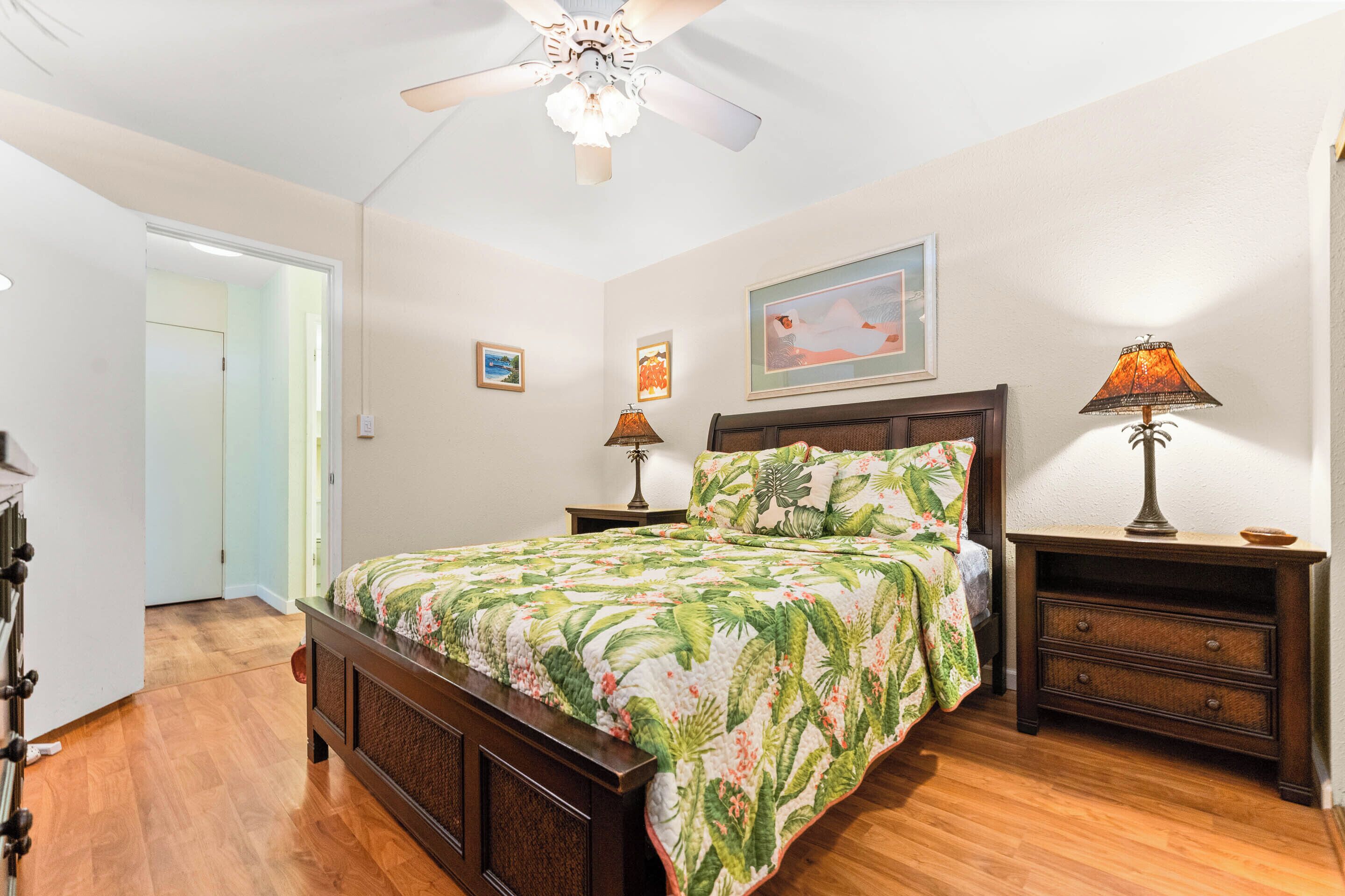 A bedroom with a wooden bed, two nightstands, a ceiling fan, and a door leading to another room.