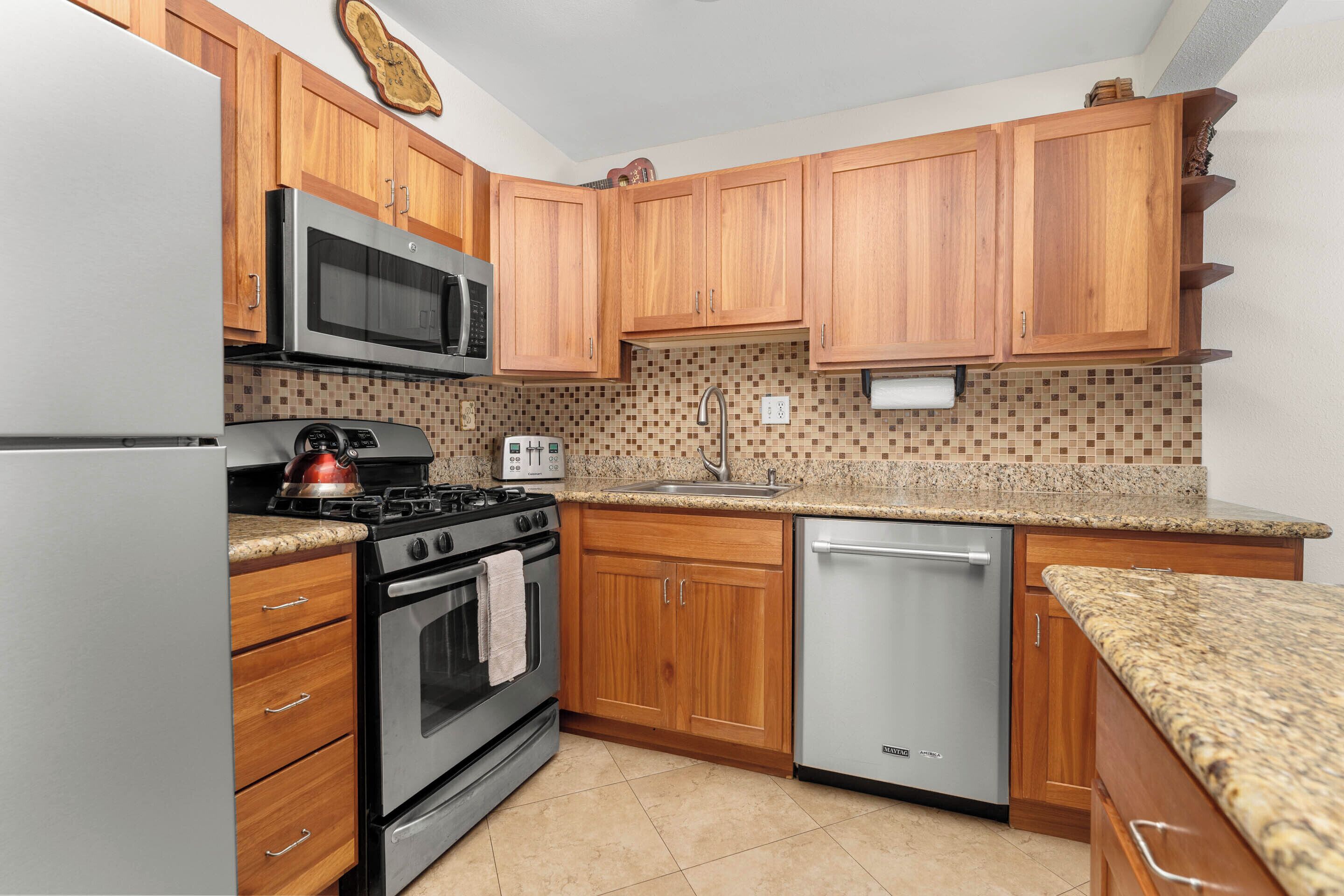 A kitchen with wooden cabinets, a stainless steel refrigerator, a microwave, a stove, a dishwasher, and a tiled backsplash.