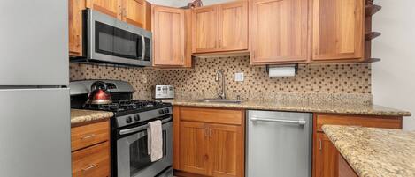 A kitchen with wooden cabinets, a stainless steel refrigerator, a microwave, a stove, a dishwasher, and a tiled backsplash.