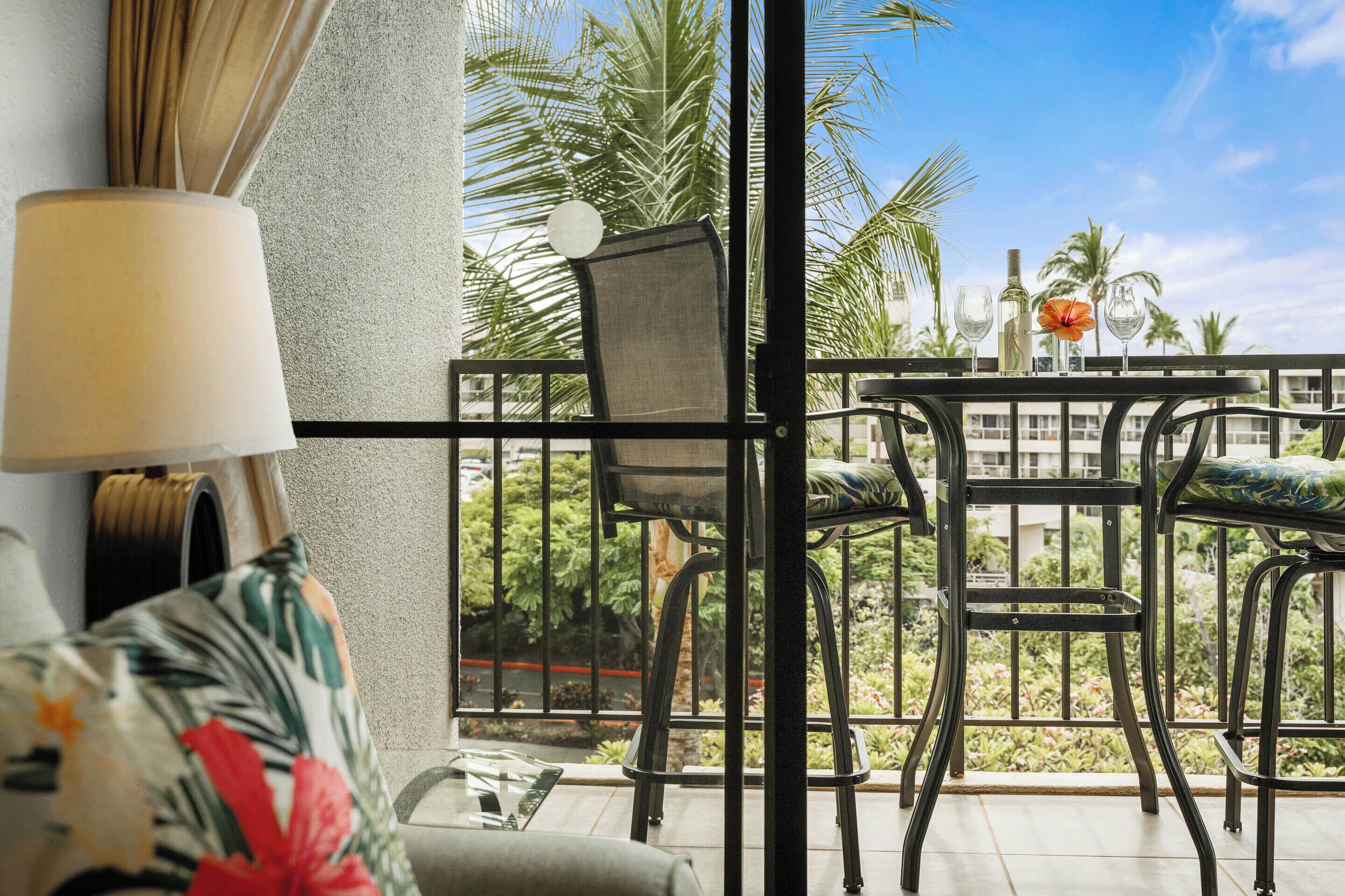 Een balkon met een tafel, stoelen, een lamp en uitzicht op palmbomen en gebouwen.