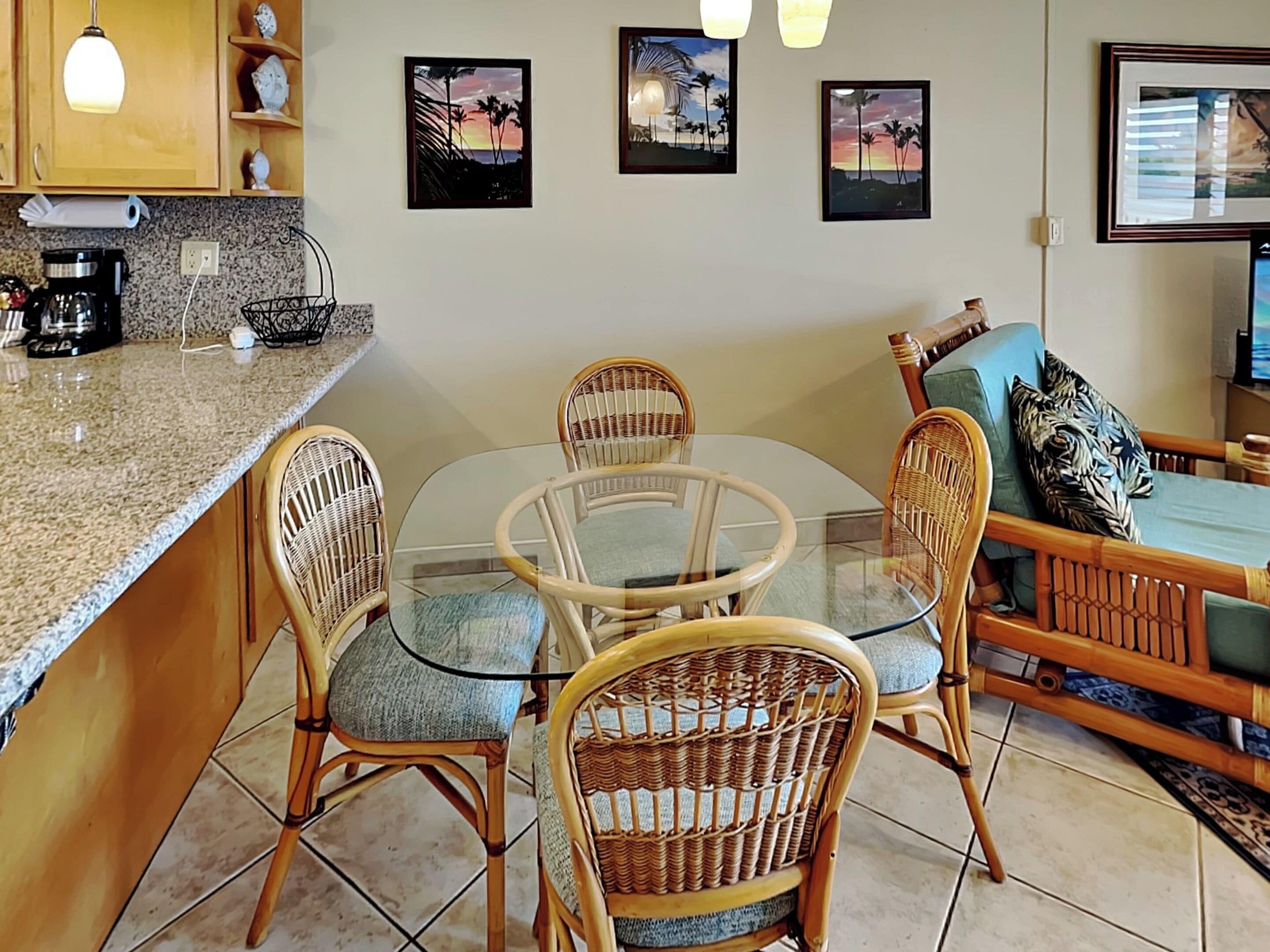 A kitchen with a round glass table, wicker chairs, a coffee maker, and a TV on a stand.