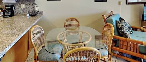 A kitchen with a round glass table, wicker chairs, a coffee maker, and a TV on a stand.