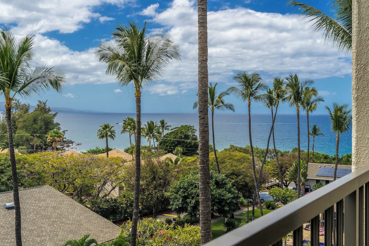 A view from a balcony overlooking a beach with palm trees and a clear sky.