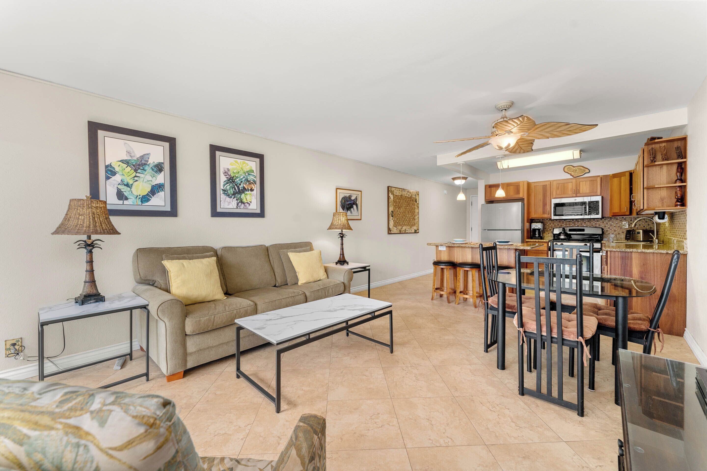 A spacious living area with a sofa, coffee table, and dining table with chairs. There is a kitchen with a microwave and cabinets.