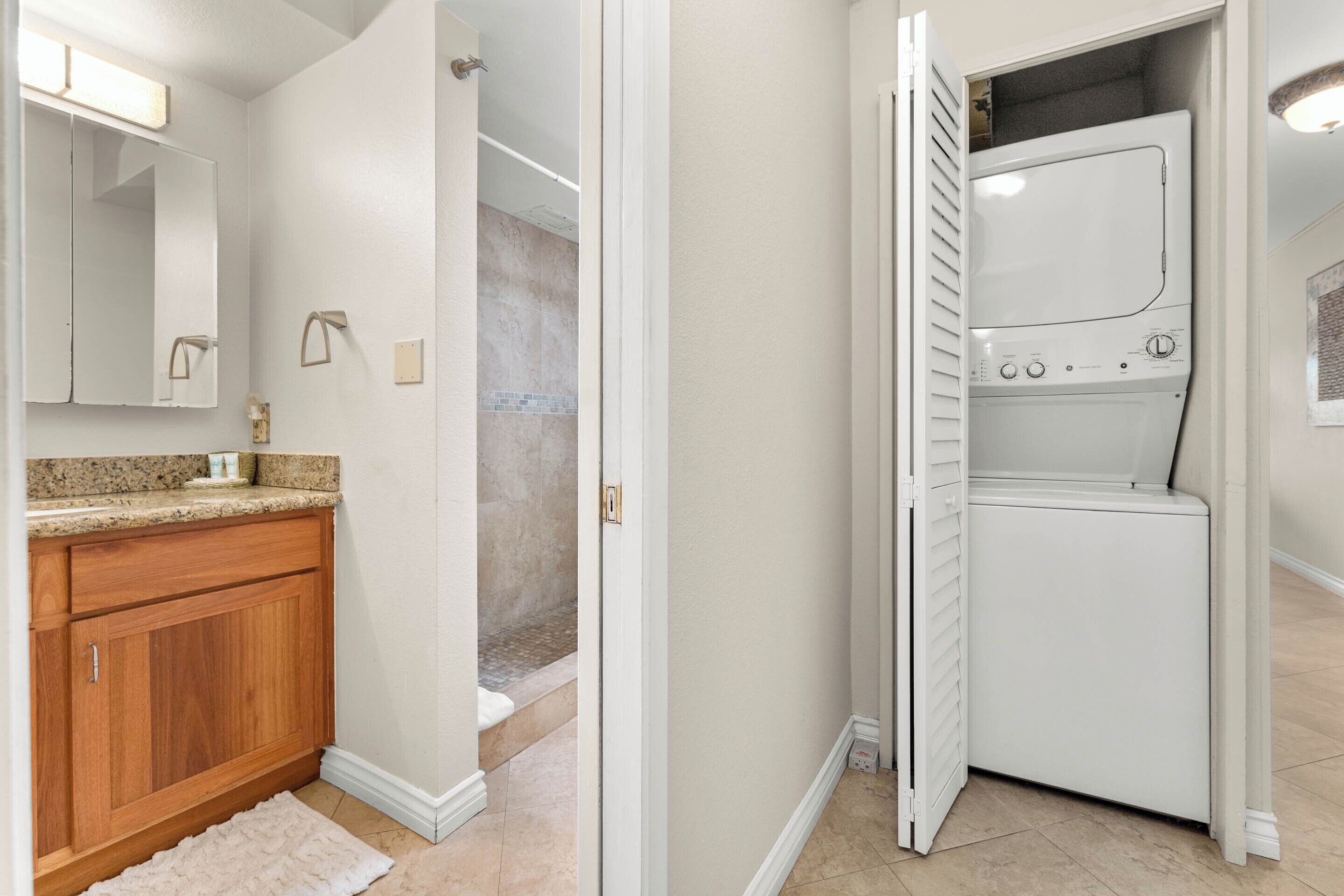 A laundry room with a washing machine, a wooden cabinet, and a mirror.