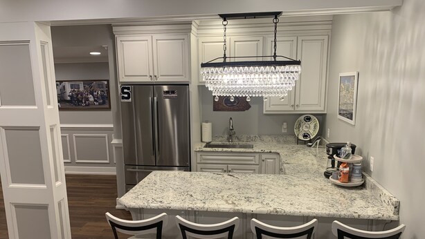A kitchen with white cabinetry, a stainless steel refrigerator, a marble countertop, and a chandelier.