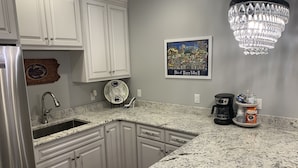 A kitchen with white cabinets, a granite countertop, a stainless steel refrigerator, a coffee maker, and a chandelier.