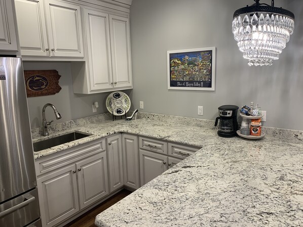 A kitchen with white cabinetry, a granite countertop, a stainless steel refrigerator, a coffee maker, and a chandelier.