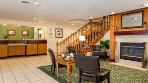 Un vestíbulo de hotel con mostrador de recepción, una escalera, una chimenea y un comedor con sillas y una mesa.