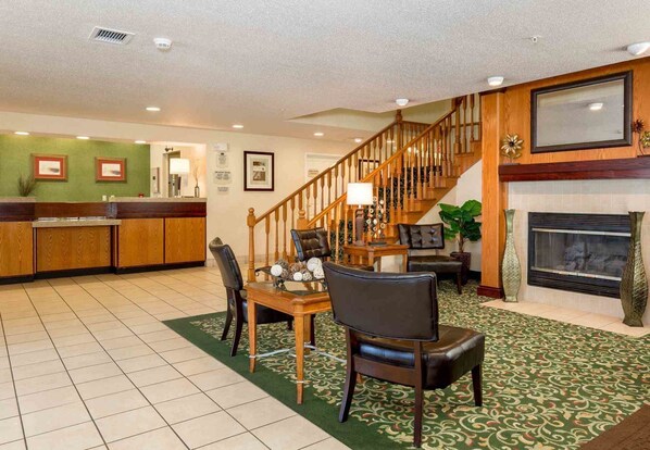 Un vestíbulo de hotel con mostrador de recepción, una escalera, una chimenea y un comedor con sillas y una mesa.