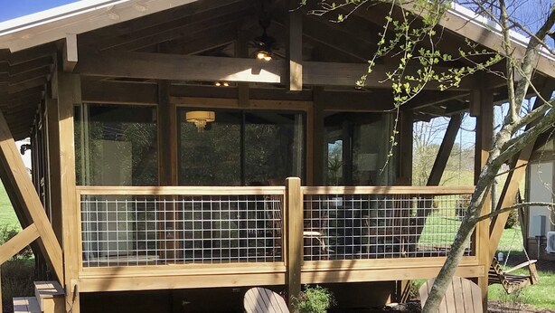 A wooden deck with a covered seating area, a fenced-in section, and a small tree in the foreground. - The Makenzee at Ridgeview. Asheville rental! Luxurious Glamping! (Alexander)