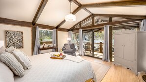 A bedroom with a large bed, a chandelier, a view of the outdoors, a dining area, and a wardrobe. - The Makenzee at Ridgeview. Asheville rental! Luxurious Glamping! (Alexander)