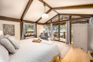 A bedroom with a large bed, a chandelier, a view of the outdoors, a dining area, and a wardrobe. - The Makenzee at Ridgeview. Asheville rental! Luxurious Glamping! (Alexander)