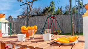 Une table de pique-nique en bois, avec une assiette d’oranges, deux tasses blanches et un verre de jus.