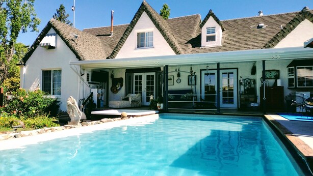 A house with a swimming pool, a covered patio, and a garden.