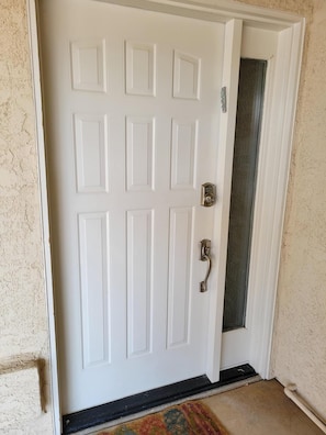 Una puerta blanca con picaporte plateado y cerradura, en una pared con textura.