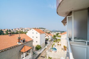 Un balcon donnant sur une ville, avec des bâtiments aux toits recouverts de tuiles rouges et un ciel dégagé.