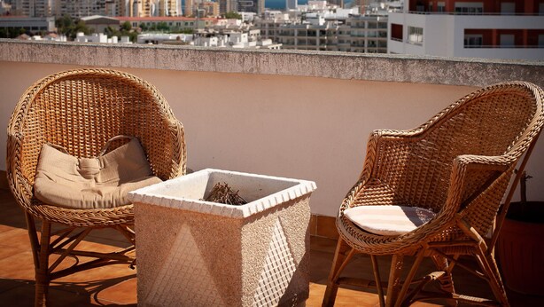 A balcony with wicker chairs and a small table, overlooking a cityscape with buildings and a clear sky. - Praia da rocha, MArina. (Portimão)