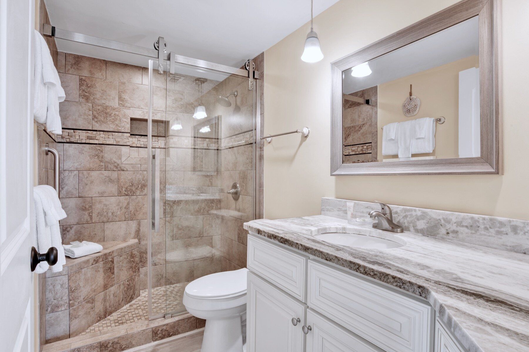 Une salle de bain avec une douche à parois de verre, des toilettes blanches et un plan de toilette en marbre avec un lavabo.