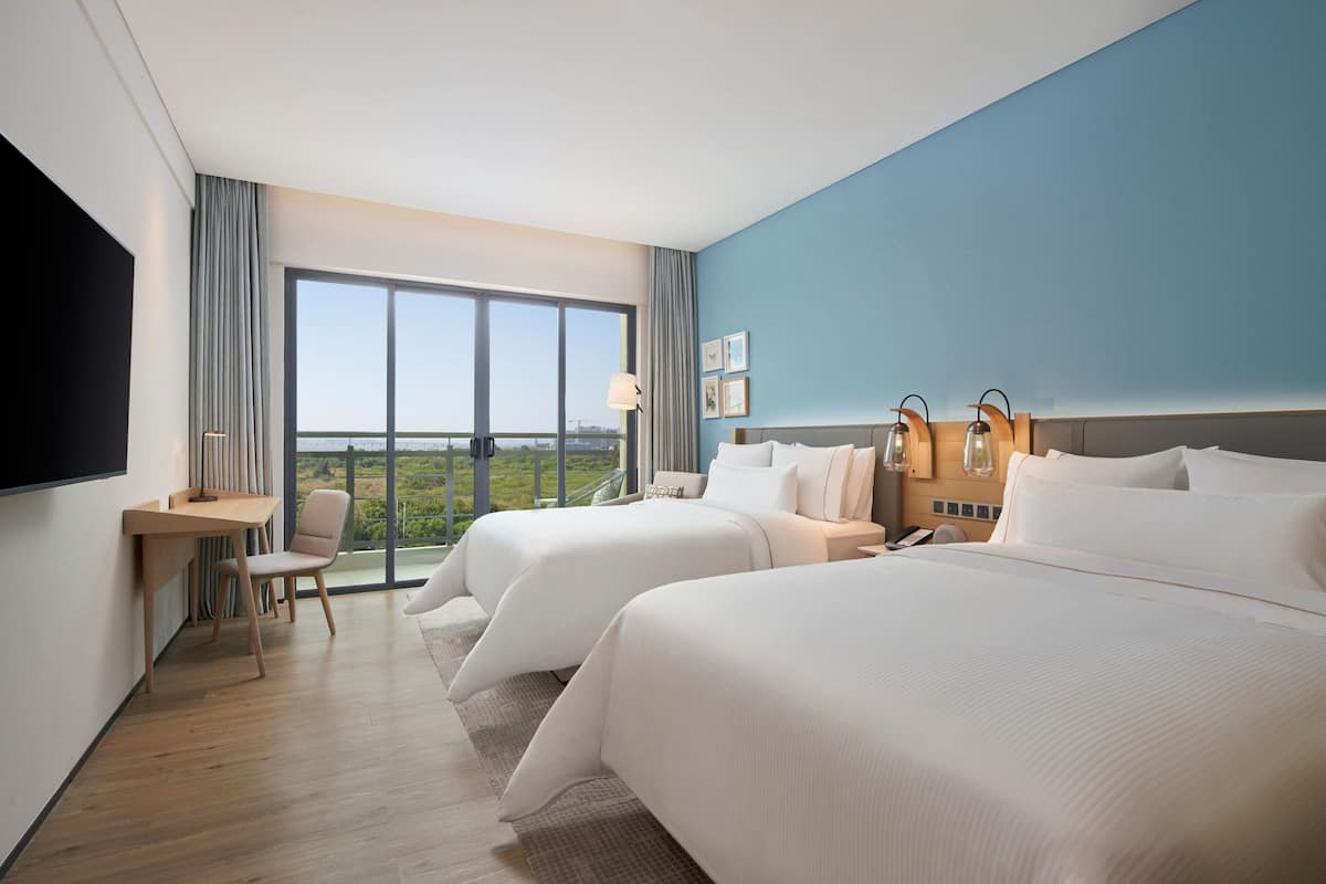 A hotel room with two beds, a desk, and a chair.
