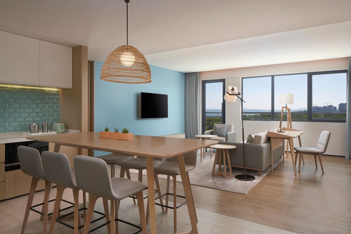 A modern living room with a dining area, a flat-screen TV, and large windows offering a city view.