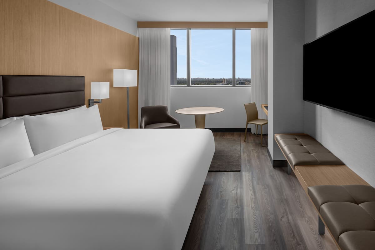 A hotel room with a large bed, a desk, a chair, a round table, and a TV.