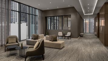 Un hall espacioso con diseño moderno, que incluye un conjunto de sofás, sillones, una mesita y una mesa de centro. Amplias ventanas ofrecen vistas de la ciudad.
