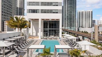 A rooftop pool area with lounge chairs and umbrellas, surrounded by tall buildings.
