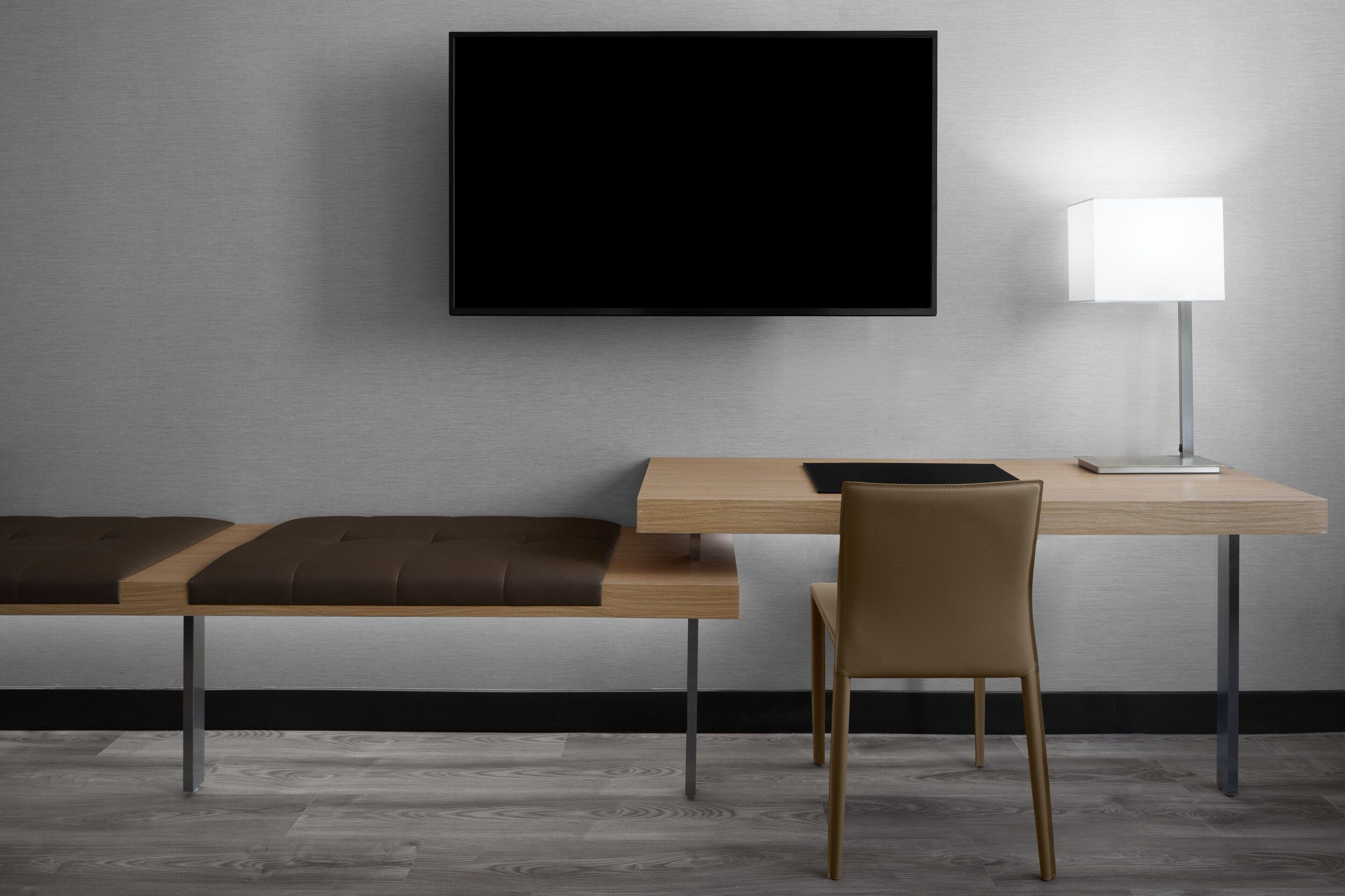 Une chambre moderne équipée d’un bureau en bois, d’un banc, d’une chaise, d’un téléviseur à écran plat et d’un lampadaire.